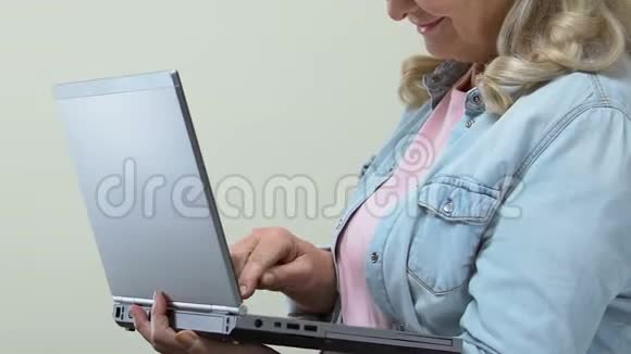 女性退休老人用笔记本电脑和微笑相机打字网上银行互联网视频的预览图