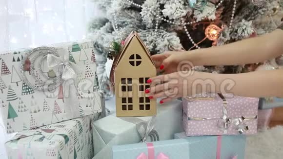 女人着红色明亮的指甲把圣诞礼物和一个纸板房子放在圣诞树下视频的预览图