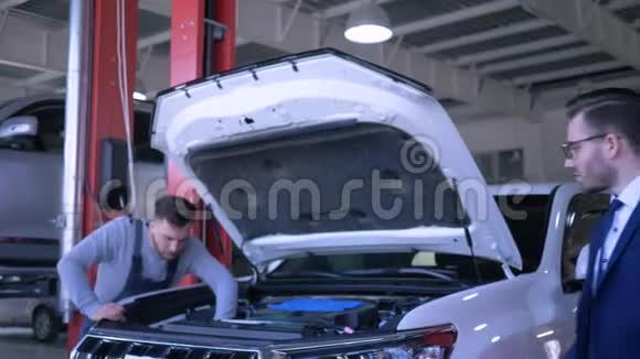 汽车修理店伤心的客户男性对汽车坏了开着引擎盖由专业师傅修理视频的预览图
