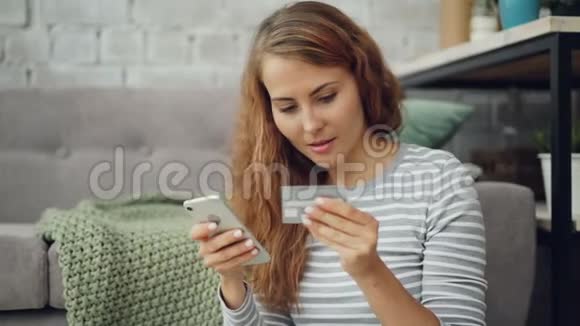 兴奋的年轻女士拿着银行卡在网上付款触摸智能手机屏幕然后开心地笑着视频的预览图