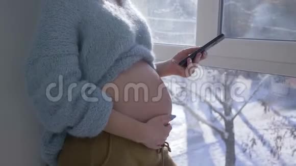 现代父母男人用手在自然光下用手机在手臂特写时抚摸孕妇的腹部视频的预览图