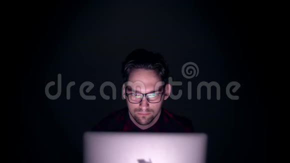 哈克晚上在一个黑暗的房间里集中精力在电脑上工作黑暗中监视器后面一个人的肖像视频的预览图
