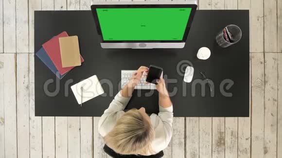 年轻的金发女人在她的工作站上的智能手机上发短信绿屏模拟显示视频的预览图
