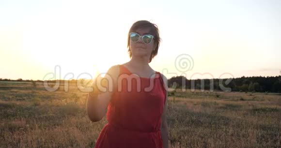 戴墨镜的漂亮女人穿着红色的裙子在一片田野里跳舞视频的预览图