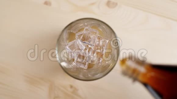 在浅棕色的木桌上倒入装有冰块的玻璃杯中的可乐汽水视频的预览图