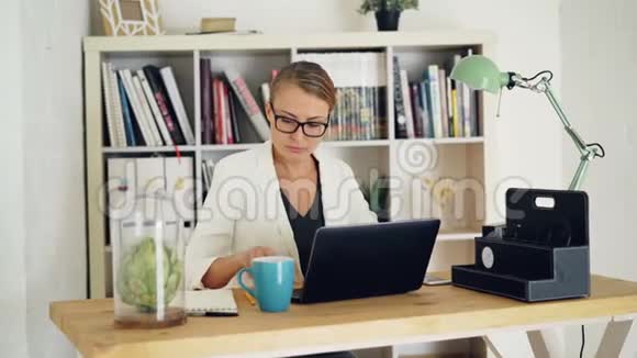 有魅力的年轻女性正在现代办公室工作坐在桌子旁使用笔记本电脑和笔记本电脑有架子的视频的预览图