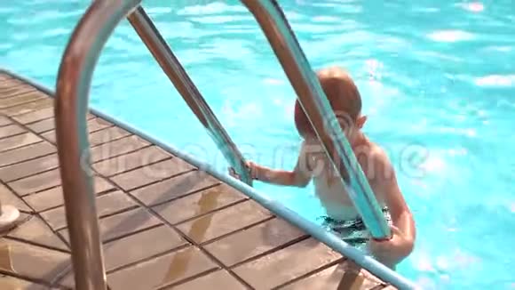 一个小可爱的男孩从夏天游泳池的水中爬楼梯视频的预览图