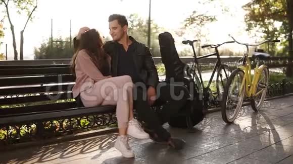 一个棕色长发的漂亮女孩坐在公园长椅上与她英俊的黑发男人拥抱在一起一幅肖像画视频的预览图