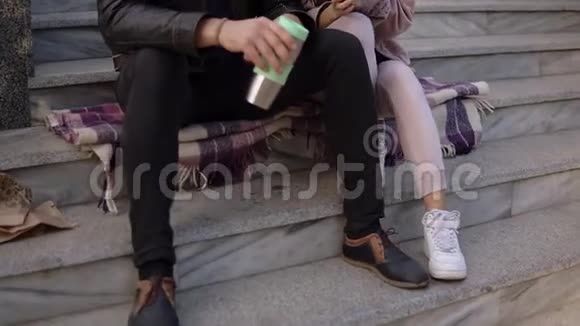 一对美丽的情侣坐在楼梯上吃羊角面包在户外喝咖啡坐在上面的画像视频的预览图