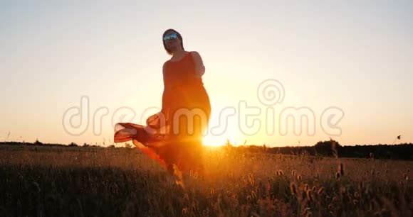一个穿着红色裙子穿着华丽优雅的女人在日落时分在田野里缓慢地跳舞视频的预览图