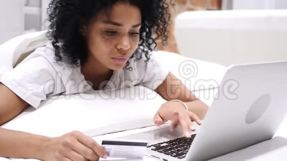 非裔美国妇女在床上成功网上购物用信用卡付款视频的预览图