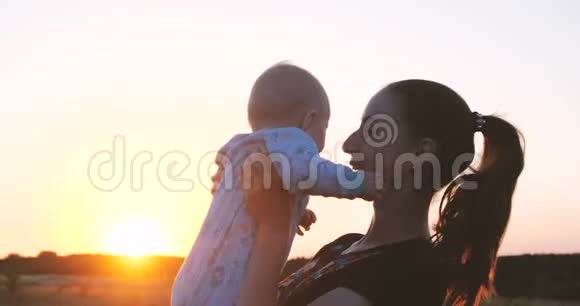 快乐的年轻女人在日落时在田野里缓慢地亲吻她的孩子视频的预览图