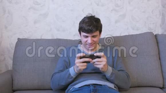 快乐的人坐在沙发上用手机玩游戏视频的预览图