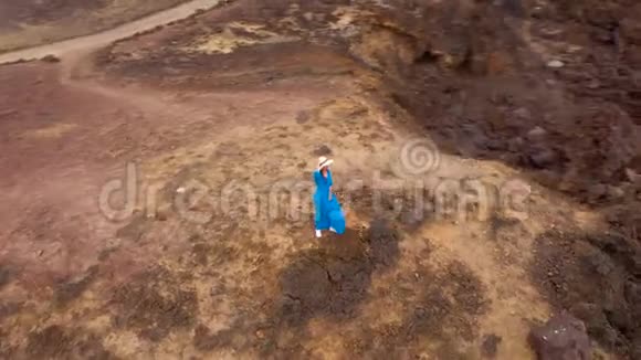 在海岸的一个保护区一位身穿漂亮蓝裙和帽子的女士站在山顶上观看空中风景视频的预览图