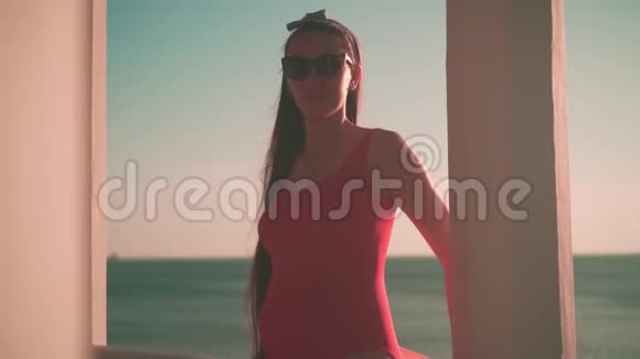 一个穿着红色的一件泳衣和眼镜的怀孕女孩站在海滩上穿着白色的混凝土凉亭视频的预览图