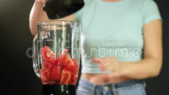 一个年轻的女人把西红柿放进搅拌机并打开它关门视频的预览图