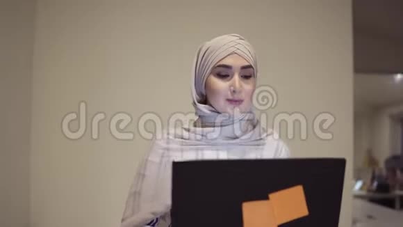 自信的阿拉伯女人戴着米色头巾手里拿着她的黑色笔记本电脑走在大厅旁雇员工作视频的预览图