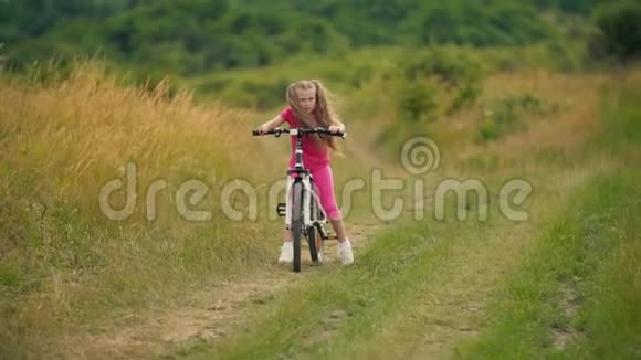女孩骑自行车在长满青草的马路上视频的预览图