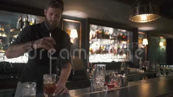 专业留胡子的酒保把朗姆酒和冰块和长金属棒混合在杯子里现代酒吧的酒吧服务员视频的预览图