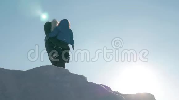 年轻的母亲在冬日夕阳的背景下把她的小男孩举得高高的视频的预览图