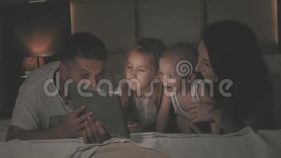 人们和家庭的观念幸福的母亲父亲小女儿和小儿子晚上躺在床上视频的预览图