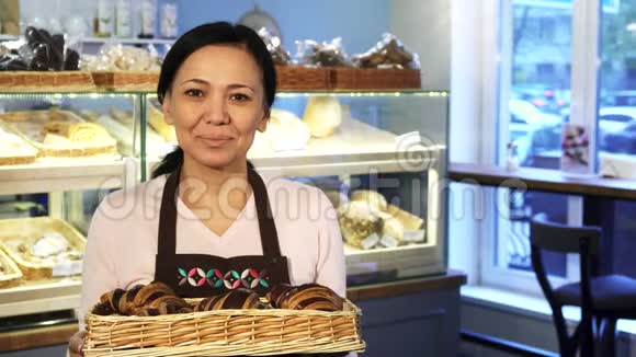成熟的女面包师拿着满满一篮子羊角面包在店里摆姿势视频的预览图