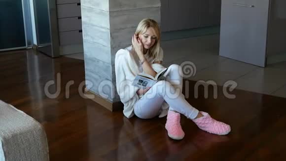 漂亮的金发女人靠在柱子上坐在地板上看书有时她会转过头来视频的预览图