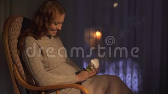 在黑暗的房间里坐在摇椅上的孕妇女士玩小袜子视频的预览图
