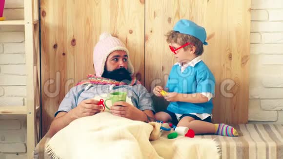 一个小医生用药片治疗他的病人一个穿着医生制服小男孩给一个长胡子的病人吃药视频的预览图