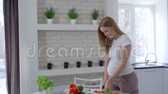 怀孕期间的营养美丽的女孩切蔬菜和吃甜椒抱着她的大肚子在厨房视频的预览图