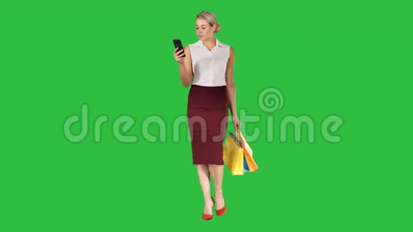 漂亮迷人的女人看着智能手机拿着购物袋走在绿色屏幕上Chroma键视频的预览图