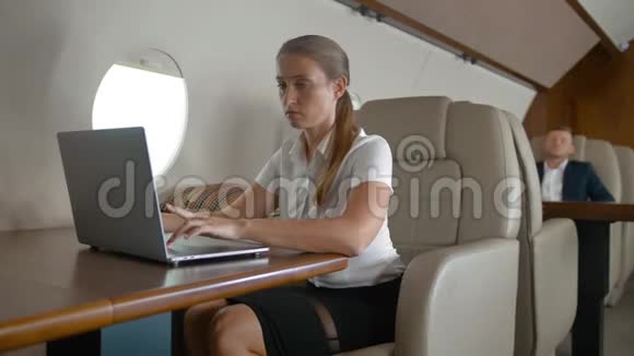 年轻的女商人在飞机的私人机舱里使用手机和笔记本电脑视频的预览图