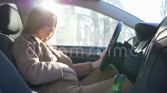 准备旅行的怀孕女孩司机穿着一条安全带坐在车轮后的背光处视频的预览图