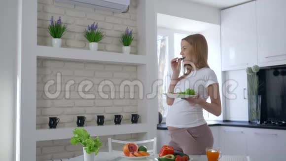 健康的营养未来的母亲手里拿着一盘沙拉吃着黄瓜抚摸着肚子视频的预览图
