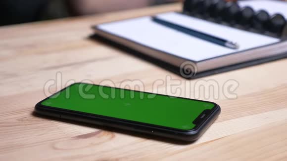 特写镜头女性手拿着一部手机绿色的屏幕放在桌子上旁边的笔记本在室内视频的预览图