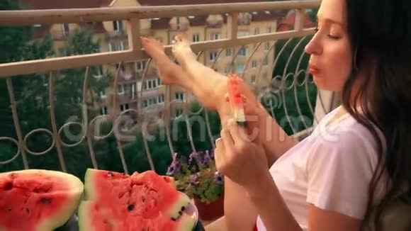美丽开朗的黑发女人在露台上吃西瓜视频的预览图