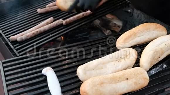 一个穿着黑色手套的街头厨师在烤架上加热面包和香肠特写镜头用木炭做饭街上的快餐视频的预览图