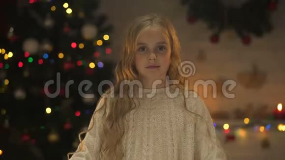 可爱的女孩用双手望着镜头做着心圣诞树在后面发光视频的预览图