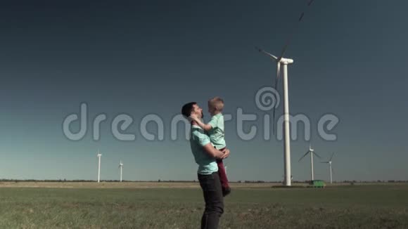 欢乐嬉戏的父子拥抱在风车旁的绿野上视频的预览图