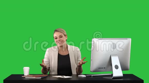 兴奋的商务女性坐在绿色屏幕上的办公桌上用相机交谈Chroma键视频的预览图