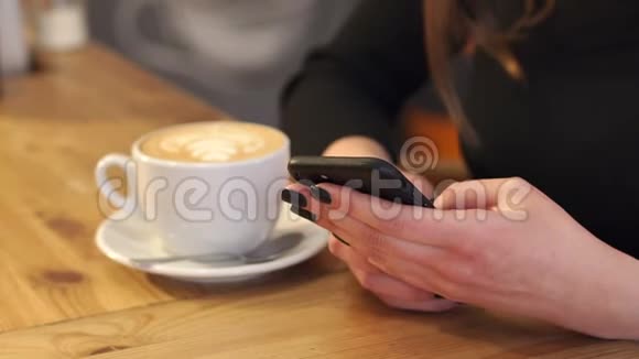 坐在桌边的一家咖啡店里手里拿着手机的女孩特写镜头视频的预览图