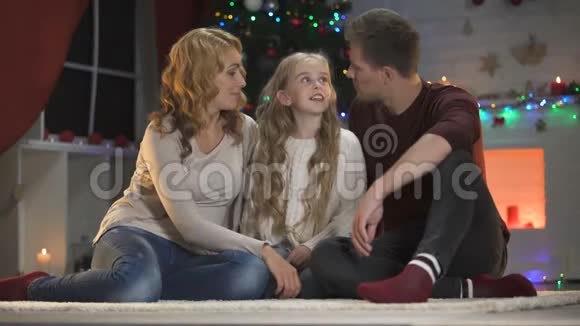 可爱的小女孩告诉快乐的父母圣诞愿望他们拥抱她微笑着视频的预览图