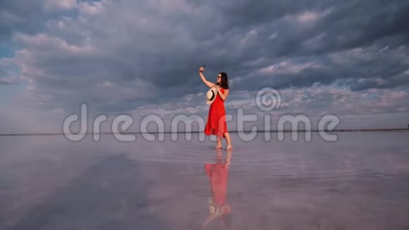 年轻女子站在一个粉红色的湖岸上自拍那里的天空被反射视频的预览图