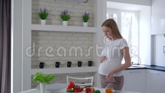 怀孕的女孩吃鳄梨手里拿着刀切蔬菜站在餐桌旁视频的预览图