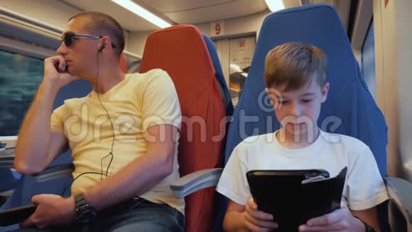 一个幸福的家庭父子俩坐在一列装有平板电脑的火车上带着智能手机坐火车旅行视频的预览图