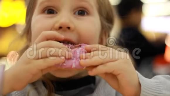 小孩嘴咬玫瑰甜甜圈特写小女孩吃甜甜圈加糖美味的甜的甜的视频的预览图