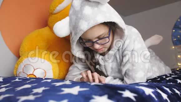 少女保暖睡衣躺在床上玩智能平板视频的预览图