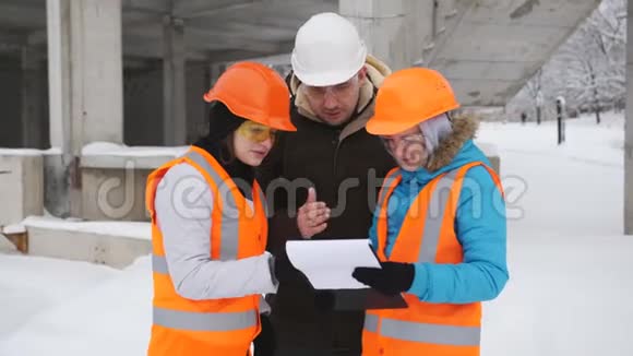 戴着安全帽的工程师和客户的两名妇女代表在一个白雪覆盖的建筑工地上交谈视频的预览图