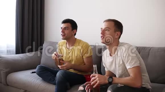 两位兴奋的成年朋友在电视上兴致勃勃地喝着啤酒在室内观看足球赛从沙发上站起来视频的预览图
