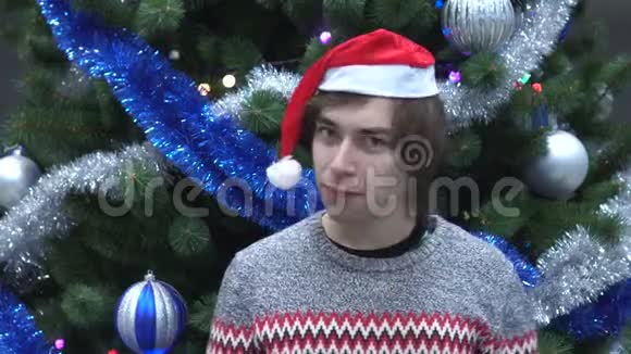 戴着圣诞帽的微笑帅哥在圣诞树背景上摇头表示不视频的预览图